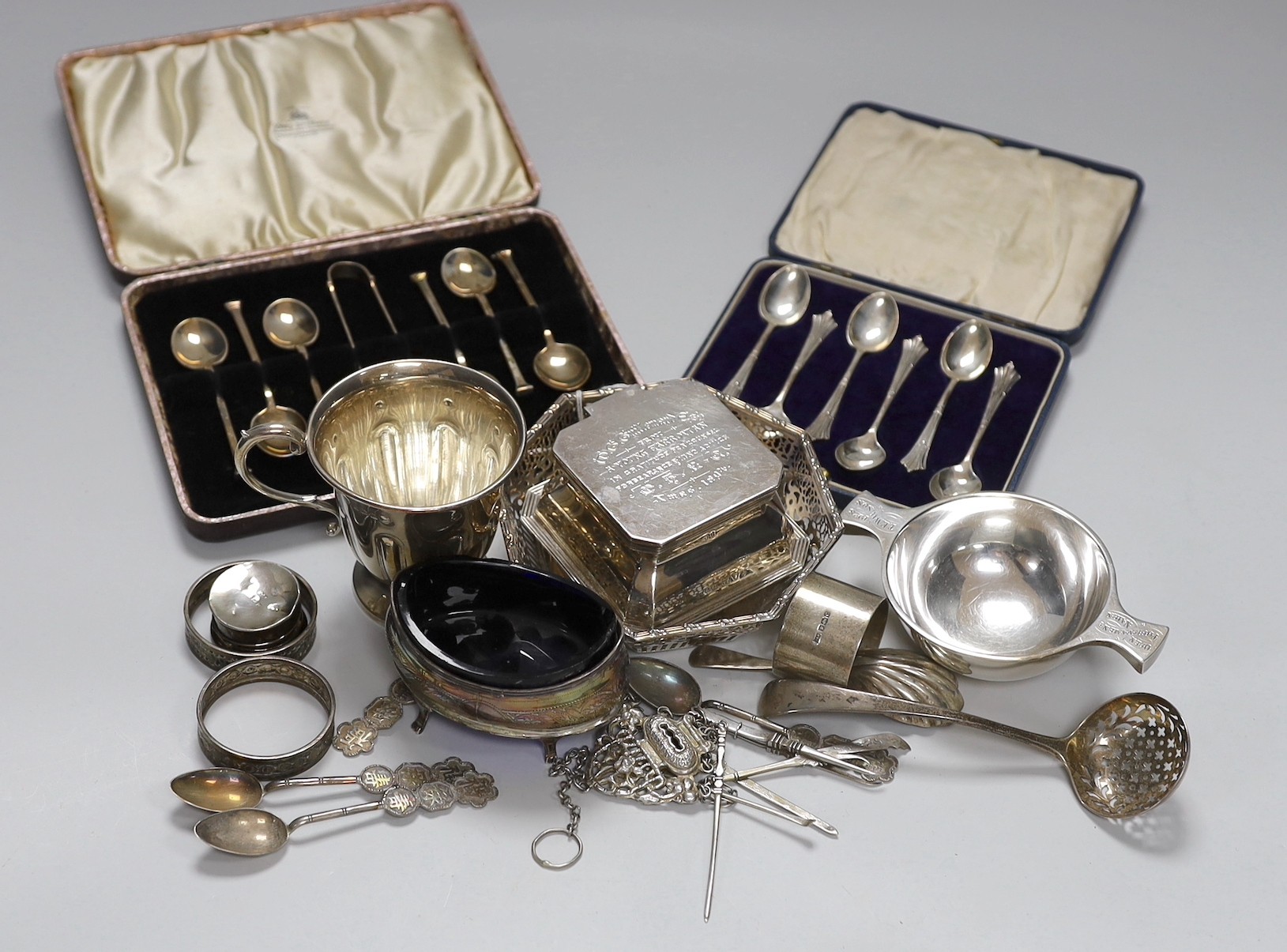 Assorted silver ware including two cased sets of six teaspoons, one with tongs, a christening mug, pierced sterling octagonal bowl, a Scottish silver quaich, inkwell, salt, three napkin rings, enamelled pill box, sifter